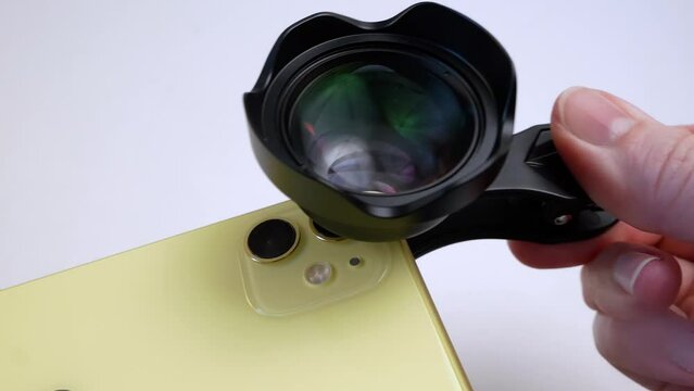 yellow smartphone with external lens  on clip on white. An additional portrait lens and clip are supplied with the mobile phone, closeup