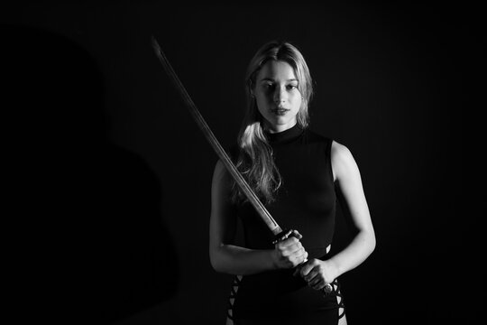 Low key portrait of young woman with katana sword in black and white