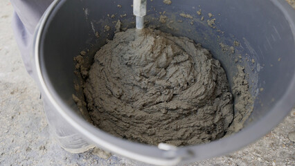 A worker mixes a solution in a bucket with a construction mixer on the street. Close-up. Mixing the solution using a construction mixer, the hands of a worker. Bucket close up.