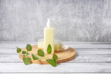 cosmetic bottles on a wooden board and a sprig of mint on a gray background