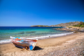 Cute dog lying on a beautiful sandy beach next to an old traditional wooden fisher boat in Syros...