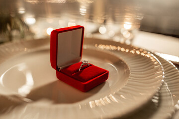 holidays, valentine's day and proposal concept - close up of engagement ring in red box on served...