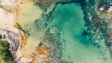 aerial aerial view from a drone towards the beach and the bay with turquoise water between the rocks and reefs of Little Bay beach in Sydney, Australia on a sunny and hot summer day.