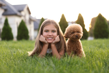 Beautiful girl with cute Maltipoo dog on green lawn in backyard