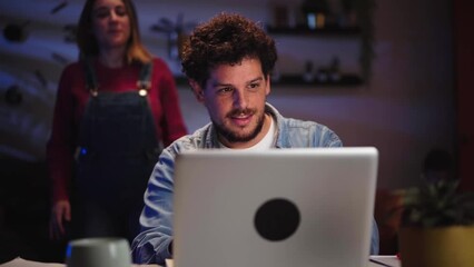 Young adult Caucasian couple affectionate looking sales together on computer in living room at night. Millennial searching vacation destination online, bookings from home using laptop. Man calls woman