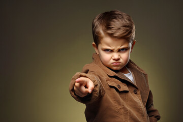 The little boy points with his finger and looks at the camera. He is angry and unhappy - obrazy, fototapety, plakaty