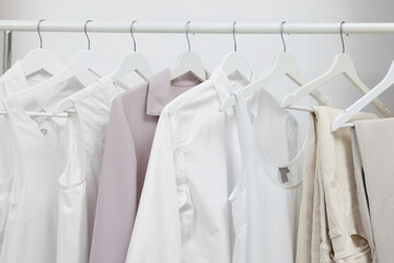 Rack with different stylish women`s clothes near white wall