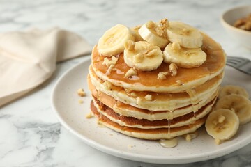 Delicious pancakes with bananas, walnuts and honey on white marble table, closeup