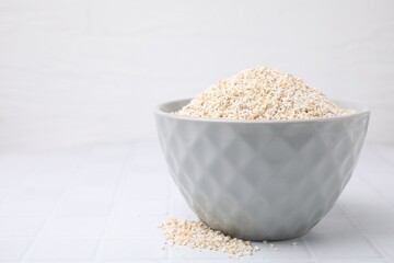 Dry barley groats in bowl on white tiled table, closeup. Space for text