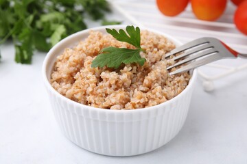 Tasty wheat porridge with parsley in bowl on white table, closeup