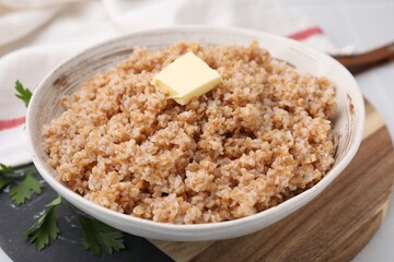 Tasty wheat porridge with butter and parsley in bowl on table, closeup