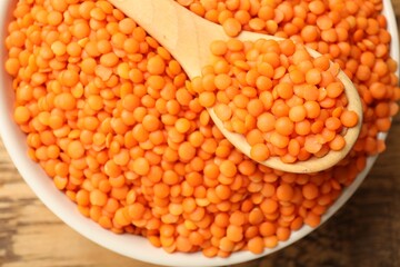 Raw red lentils in bowl and spoon on wooden table, top view