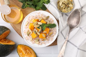 Tasty wheat porridge with pumpkin and mint in bowl served on table, flat lay