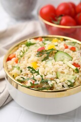 Cooked bulgur with vegetables in bowl on white tiled table, closeup