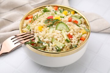 Cooked bulgur with vegetables in bowl on white tiled table, closeup