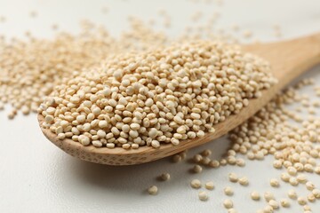 Spoon with dry quinoa seeds on white table, closeup