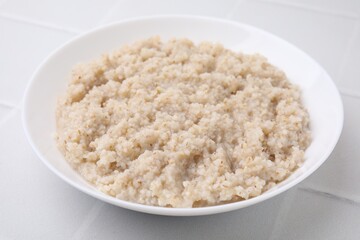 Delicious barley porridge in bowl on white table, closeup