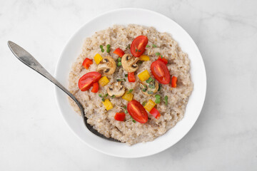 Delicious barley porridge with vegetables and microgreens in bowl served on white table, top view