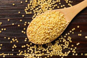 Spoon with millet groats on wooden table, top view