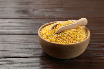 Millet groats in bowl and scoop on wooden table, space for text