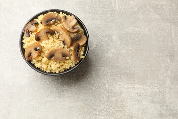 Delicious bulgur with mushrooms in bowl on gray table, top view. Space for text