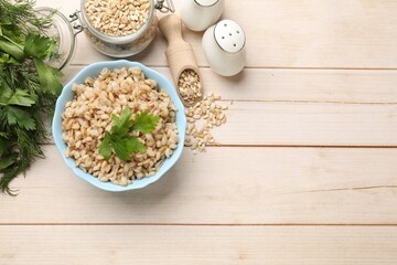 Delicious pearl barley with parsley served on wooden table, flat lay. Space for text