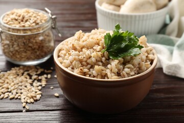 Delicious pearl barley with parsley in bowl on wooden table