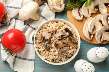 Delicious pearl barley in bowl served on light blue wooden table, flat lay