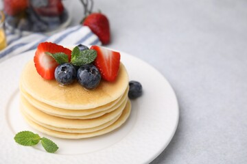 Delicious pancakes with strawberries, blueberries and honey on light grey table, closeup. Space for text