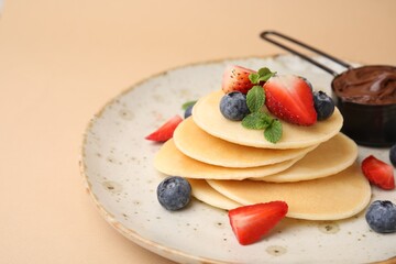 Delicious pancakes served with berries and chocolate spread on beige background, closeup. Space for text