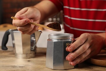 Man putting ground coffee into moka pot at wooden table indoors, closeup