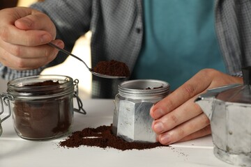 Fototapeta na wymiar Man putting ground coffee into moka pot at white wooden table indoors, closeup