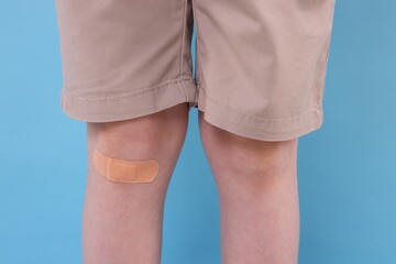 Little boy with sticking plaster on knee against light blue background, closeup