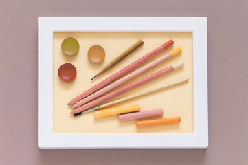 Naklejka premium Drawing and creativity as a hobby. Pencils, watercolor paints, brush and pastel sticks in warm pink and peach tones in a white frame. Shades of trendy color Peach Fuzz. Flat lay, close-up, top view