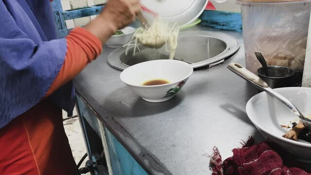 Preparing chicken noodles. View of a penjual mie ayam bakso or meatball chicken noodle seller who is making chicken noodles for the buyer. Selective focus.