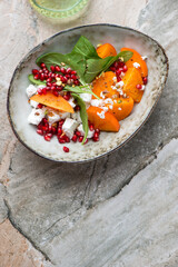 Bowl with fresh persimmon, goat cheese, spinach and pomegranate salad, above view on a grey granite background, vertical shot with space