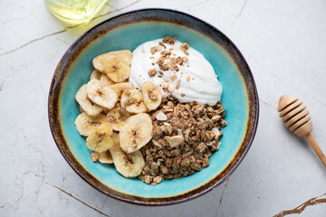 Turquoise bowl with granola, banana chips and yogurt, horizontal shot on a white granite...
