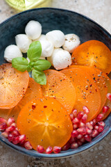 Fresh sliced persimmon with mini mozzarella balls and pomegranate seeds, vertical shot, close-up