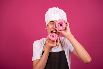 Young funny chef and pastry chef is cooking. Pink background.