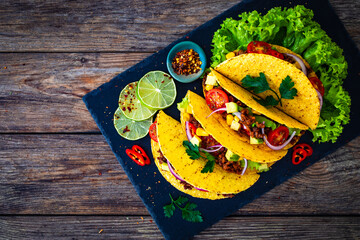 Tacos with ground beef, avocado, corn and fresh vegetables on wooden table 
