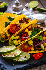 Tacos with ground beef, avocado, corn and fresh vegetables on wooden table 