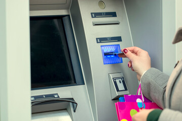 Close-up view of female with shopping bags using her credit card at the ATM