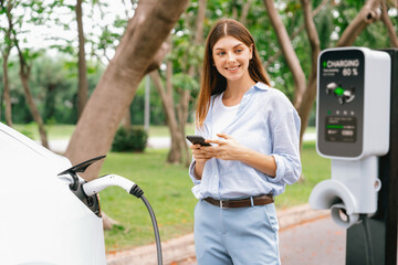 Young woman using smartphone online banking application to pay for electric car battery charging...