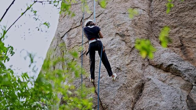 A young Indian girl is climbing or rappelling down the rock mountain