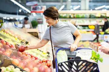 Positive woman chooses ripe red apples on grocery store window