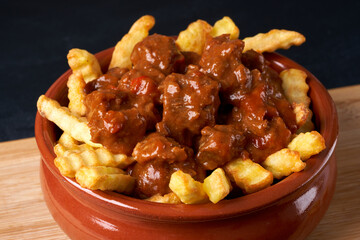 Fried fries with goulash in a red plate.