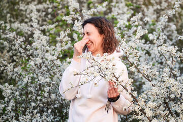 Woman allergic suffering from seasonal allergy at spring in blossoming garden at springtime. Young...
