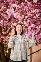 Woman allergic suffering from seasonal allergy at spring. Young happy woman applying allergy drug, posing in blossoming garden at springtime. Antihistamine medication concept