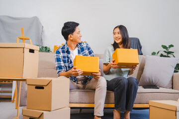 Asian couple is unpacking boxes in a festive living room with a Christmas tree, showing surprise and happiness.