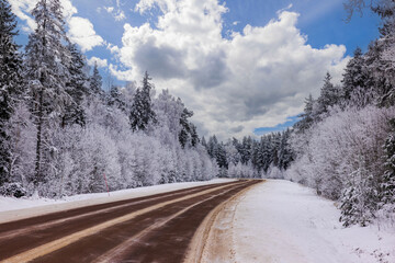 View of highway running alongside winter forest covered in snow, with road markers against backdrop...
